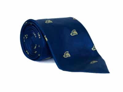 Rolled royal blue silk tie featuring a repeating cream BASC crest pattern, displayed on a white background to showcase the fabric texture and design.