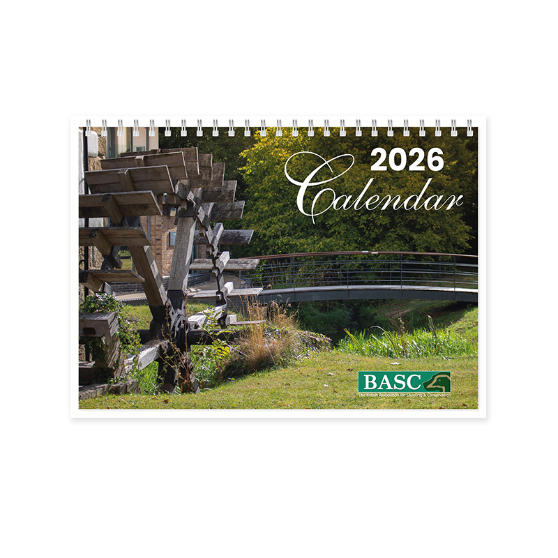 Cover of 2026 calendar featuring an outdoor scene with a wooden waterwheel, a modern pedestrian bridge, lush greenery, and partially visible buildings. '2026 Calendar' text in white script at the top right, with the BASC logo at the bottom right