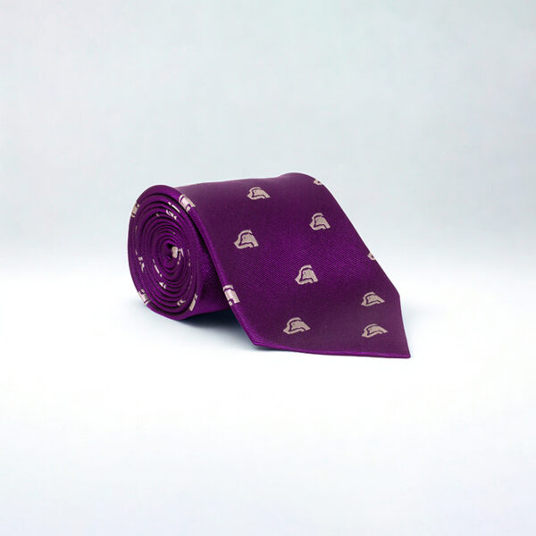 A deep purple silk tie, featuring the BASC masthead logo embroidered in silver, neatly rolled up on a white background. 