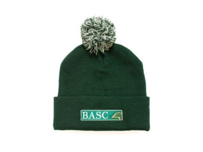 Dark green knitted bobble beanie hat with fold-over cuff and two-tone green and white pom-pom. Embroidered BASC logo on the front, suitable for countryside activities and winter wear.